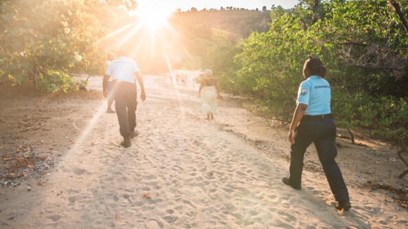 Alors que le soleil se couche, deux réservistes patrouillent de dos le long de la plage tandis que plus loin des locaux se promènent de dos.