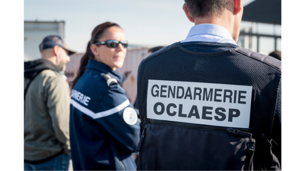 Deux gendarmes, l'un de dos et l'une de côté en flou. Celui de dos porte une chassuble avec noté dessus : Gendarmerie OCLAESP