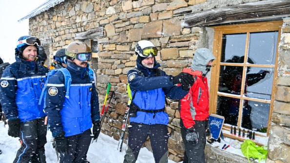 quatre gendarmes, d'autres personnes derrière et un homme en rouge devant un chalet. un gendarme pointe un pistolet