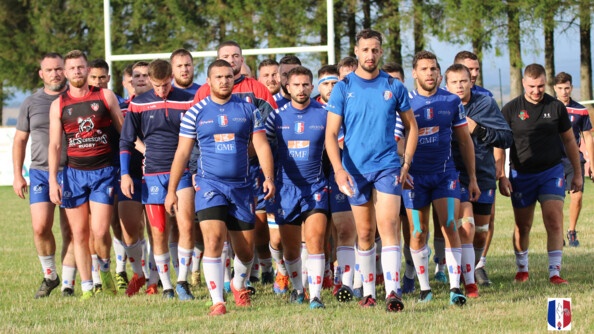 environ 25 hommes en tenue de rugby s'avancent, marchant en groupe, de face; sur un terrain d'herbe. Derri&egrave;re eux, les poteaux