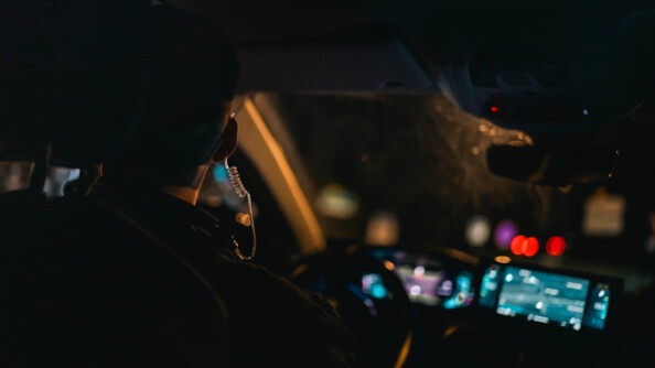 Un gendarme de dos dans une voiture. Il fait nuit et sombre.