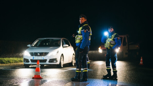 Deux gendarmes sur la droite contrôlant des voitures. On peut voir une voiture blanche à gauche de l'image.