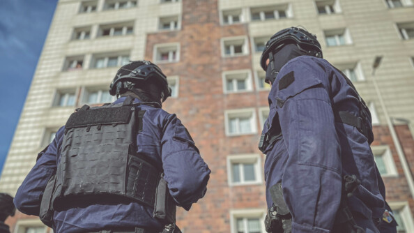 Deux gendarmes en tenue d'intervention devant une barre d'immeuble.