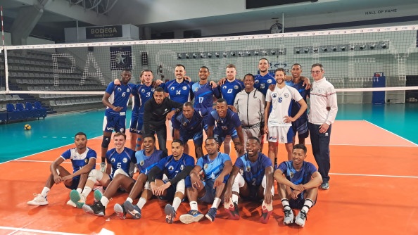 Un groupe de sportif debout et assis devant u filet de voleyball dansun gymnase