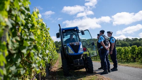 Trois gendarmes échangent avec un viticulteur dans son tracteur.