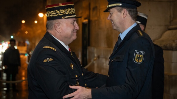 Un g&eacute;n&eacute;ral de gendarmerie francais et un policer allemand se serre la main avec chaleur, de nuit, en ville, sous la pluie