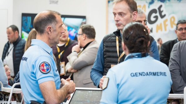 Deux gendarmes sont entrain de parler avec un agriculteur. Dans le fond, on voit plusieurs autres personnes, discuter entre elles.