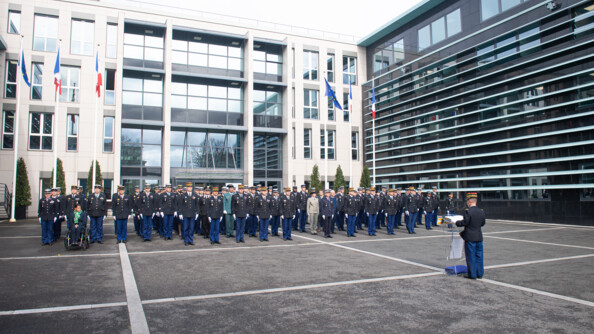 Une centaine de personnels de la direction générale de la gendarmerie en rang dans la cour d'honneur lors de la lecture de l'ordre du jour par le major général que l'on voit de dos.