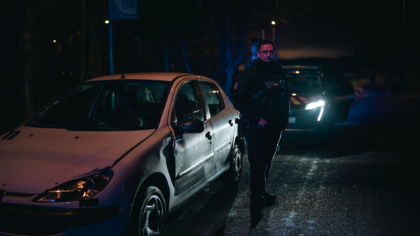Un gendarme à côté d'un véhicule accidenté. Il fait nuit et sombre.