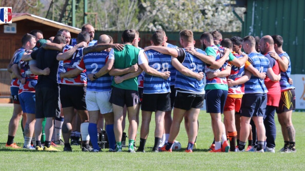 Environ 25 hommes en tenue de rugby, de diff&eacute;rentes couleurs, en cercle, se tiennent par les &eacute;paules et le dos