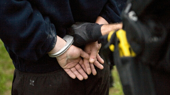 Homme de dos menotté et tenu par un agent des forces de l'ordre.