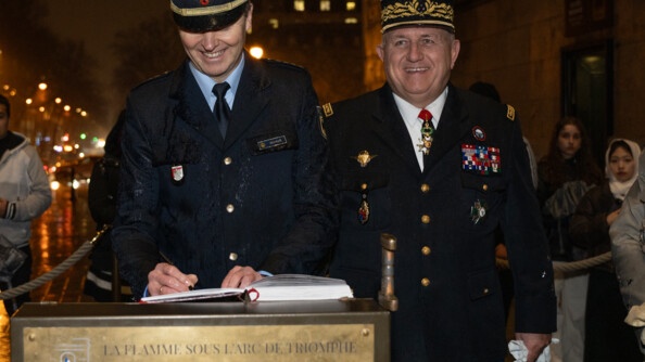 Un policier allemand signe un registre, de nuit, sous la lpluie et les lumi&egrave;res de la ville. A sa droite, un g&eacute;n&eacute;ral de gendarmerie souriant