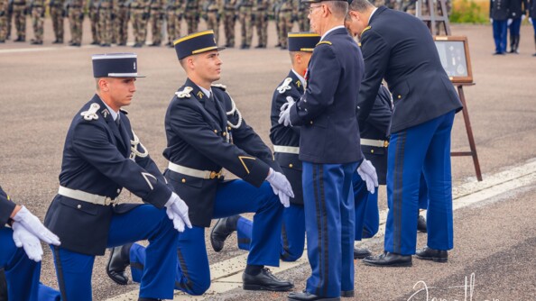 4 élèves-gendarmes genou à terre dont deux officiers généraux retirent les galons de vareuse