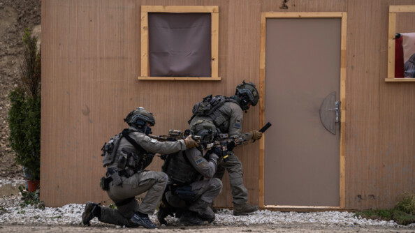 Trois militaires du GIGN en tenue kaki s'appr&ecirc;tent &agrave; mettre des explosifs au pied d'une porte d'un pr&eacute;fabriqu&eacute; en bois