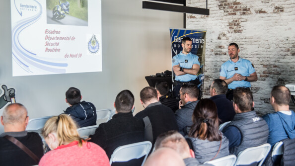 Devant un groupe assis sur des chaises, deux gendarmes présentent un power point projeté au mur sur la gauche