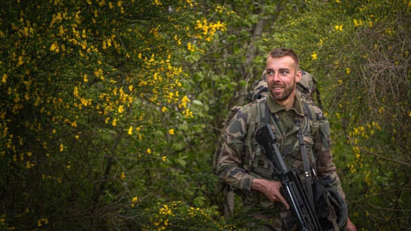Un sous lieutenant pris de côté avec son FAMAS, sortant de la pause dîner et souriant