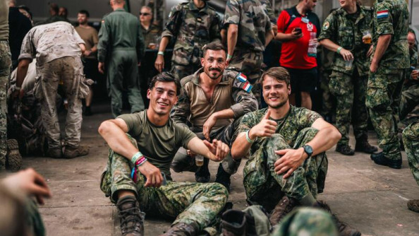 Trois jeunes militaires, en trellis kaki, assis au sol, posent, souriants, face à l'objectif. Celui du milieu porte à l'épaule un écusson représentant le drapeau français