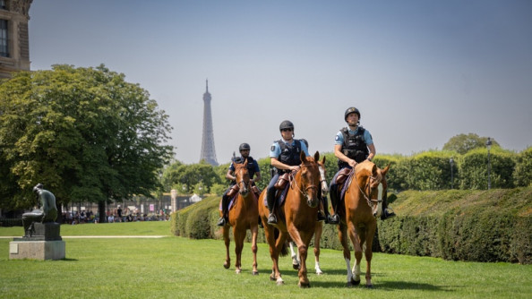 Trois gendarmes à cheval patrouillent à Paris. Ils traversent un parc. On aperçoit la Tour Eiffel dans leur dos.