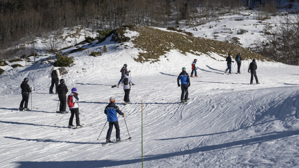 Deux gendarmes sur la piste de ski entourée d'une dizaine de skieurs, tous de dos, remontant une faible piste au bord de la forêt