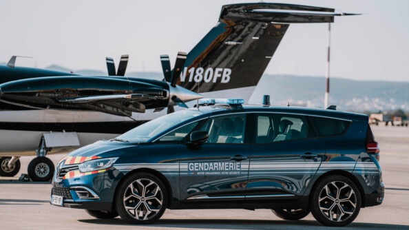 Une voiture bleue marine, portant sur la portière l'inscription "Gendarmerie - Notre engagement, votre sécurité", est garée sur la piste d'un aéroport, devant un petit avion d'affaires de couleur noire et blanche