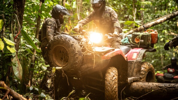 Gendarme faisant passer son quad au dessus d'un tronc. Ses feux avant sont allumés.