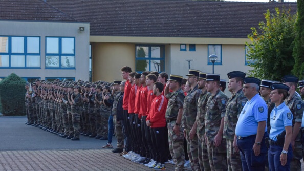 Vue de trois-quarts face sur les cadres de l'école, les sportifs et les élèves gendarmes sur la place d'armes, au garde-à-vous.