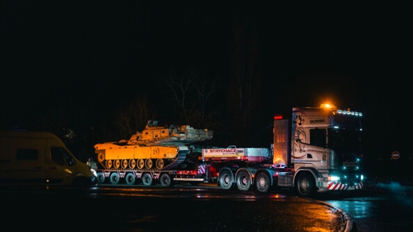 Départ du convoi. Photo du camion transportant un char. Il fait nuit et il pleut.