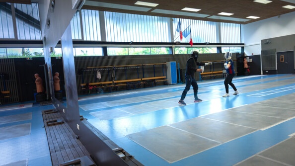 Dans le reflet d'un miroir mural deux escrimeurs s'affrontent et l'un pare l'assaut