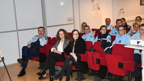 Plsieurs gendarme,s ainsi que la Déléguée interministérielle à l’aide aux victimes (DIAV), Alexandra Louis, sont assis sur des sièges rouges, écoutant une présentation.