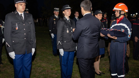 Gérald Darmanin remet une médaille à une gendarme au milieu de ses camarades en vareuse, à droite un pompier présente le coussin des médailles