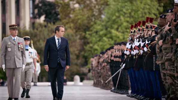 Le ministre des Armées, Sébastien Lecornu, marche sur une esplanade, le visage tourné vers des militaires en faction se trouvant sur sa gauche.