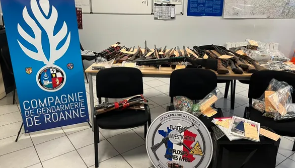 Des saisies d'armes et de munitions sous scellés sur une table, à gauche le kakémono de la compagnie de gendarmerie de Roanne, au centre la rondache du Plateau d'investigation explosifs armes à feu