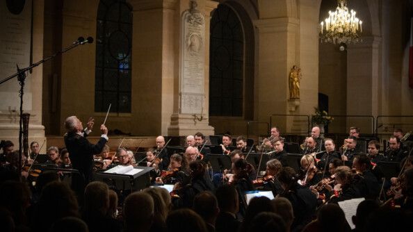 Vue deface des musiciens de l'orchestre de la Garde républicaine dans la cathédrale Saint-Louis aux Invalides à Paris. En premier plan, le public est visible.