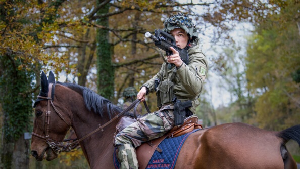 Un cavalier de la garde en treillis, casque sur la tête, sur sa monture, au milieu des bois, vise avec son Famas.