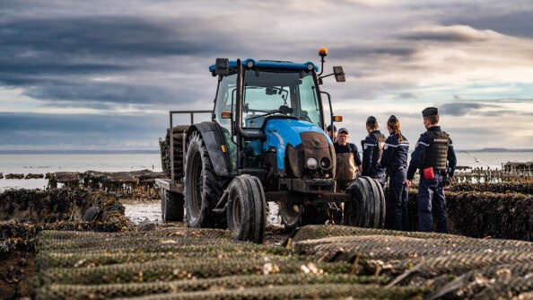 trois gendarmes parlent avec deux hommes dans un parc ostréicole près d'un tracteur bleu