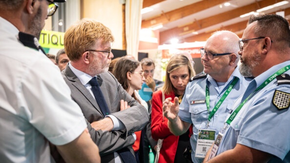 de profil regardant vers la droite, en complet gris et les bras croisés, le ministre de l'agriculture. Face à lui deux gendarmes. Derrière eux les visiteurs