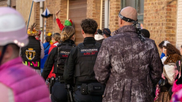 La photo repr&eacute;sente deux gendarmes, de dos, marchant dans la rue aux c&ocirc;t&eacute;s de carnavaleux d&eacute;guis&eacute;s, lors du carnaval de Bergues