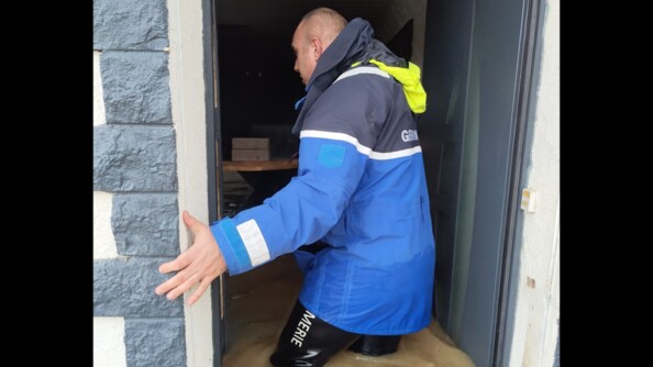 Un gendarme dans l'encablure d'une porte ouverte. L'eau monte au niveau de sa taille.