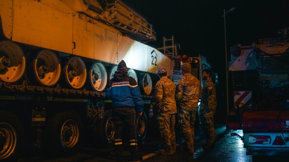 Une gendarme et des militaires américains inspectent un des chars. Il fait nuit et sombre.