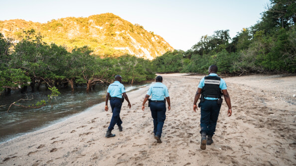 Trois réservistes de dos patrouillent sur la plage déserte.