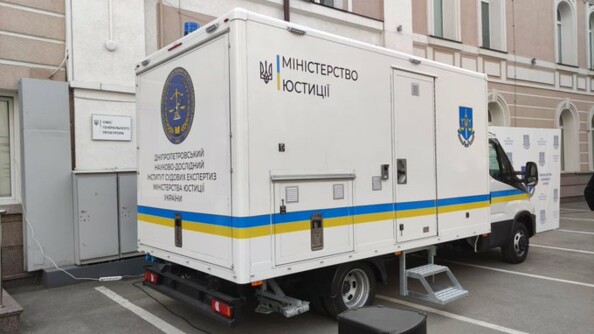 Un camion blanc avec un liseré aux couleurs du drapeau ukrainien et portant des inscriptions dans la langue du pays, garé sur le parking d'un bâtiment.