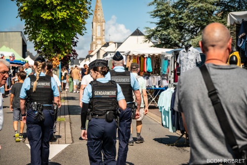 Trois gendarmes de dos patrouillant à pied dans un marché de village.