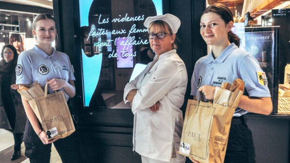 Devant la devanture d'un magasin Paul, une employée se tient au coté de deux gendarmes. Derrière elles, un spot indique sur un écran "les violences faites aux femmes sont l'affaire de tous"