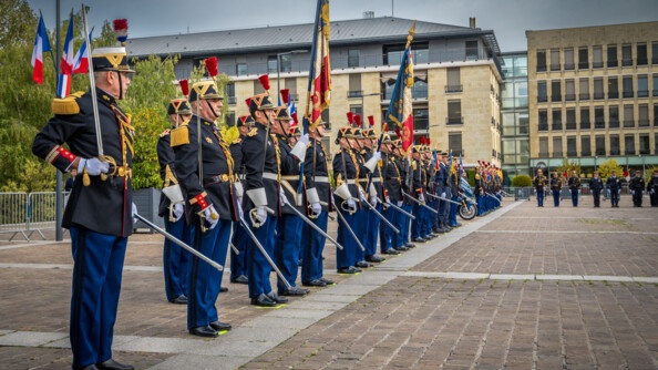 Des gardes de la garde républicaine en tenue sont alignés sur un grand parvis, tenant des drapeaux