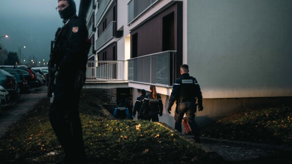 Des gendarmes s'approchent d'un immeuble, la nuit, dans lequel ils s'appr&ecirc;tent &agrave; p&eacute;n&eacute;trer, tandis qu'un autre militaire se tient en faction devant le b&acirc;timent, surveillant ainsi les abords.