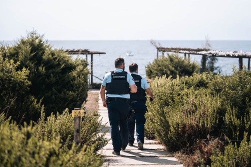 Deux gendarmes marchent, dos à l'objectif, l'un derrière l'autre, sur un sentier menant à la mer.