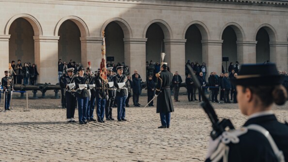 Dans une cour, la garde du drapeau de la gendarmerie, devant un aute gendarme en grand uniforme. autour de la cour, des civils