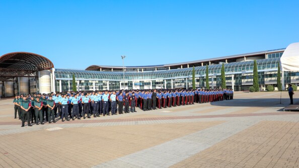 Les stagiaires sont en rangs sur la place d'arme de l'école des carabiniers. Ils sont triés par gendarmerie. Un cadre leur parle avec un micro sur une estrade.