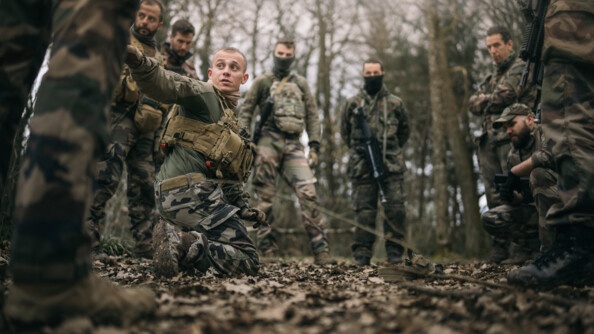 Une dizaine de gendarmes et militaires en treillis dans la forêt autour d'un qui explique la manoeuvre