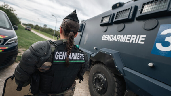 Une gendarme mobile de dos. A sa droite un véhicule blindé Centaure.